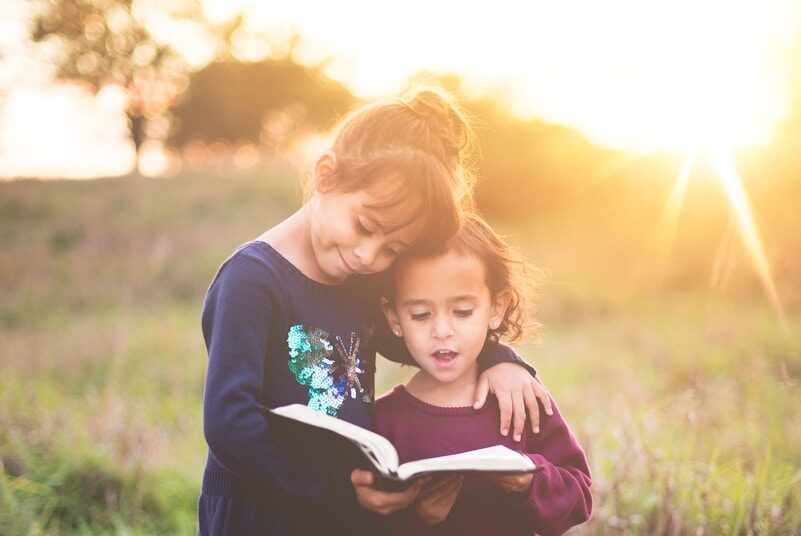 girl's left hand wrap around toddler while reading book during golden hour